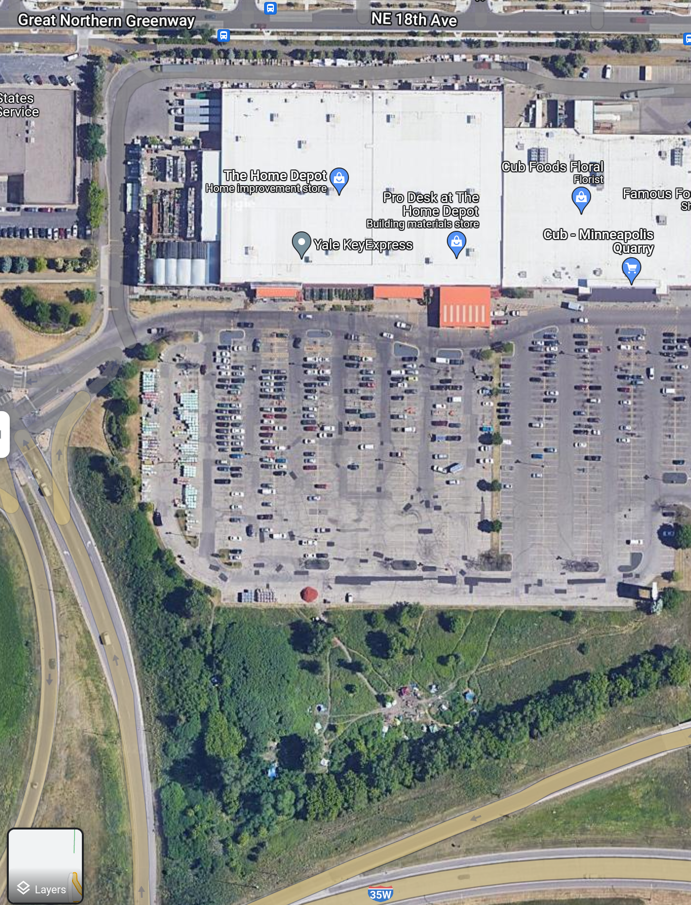 An overhead satellite image of a large parking lot, with the tents of Quarry Encampment to the South (at the bottom of the image, below the parking lot and above 35W) and The Home Depot and Cub buildings labeled to the North, beneath Great Northern Greenway / NE 18th Ave.