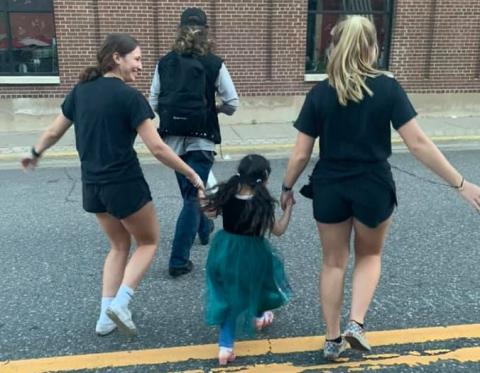 Two young restaurant workers walking with a 4-year-old girl